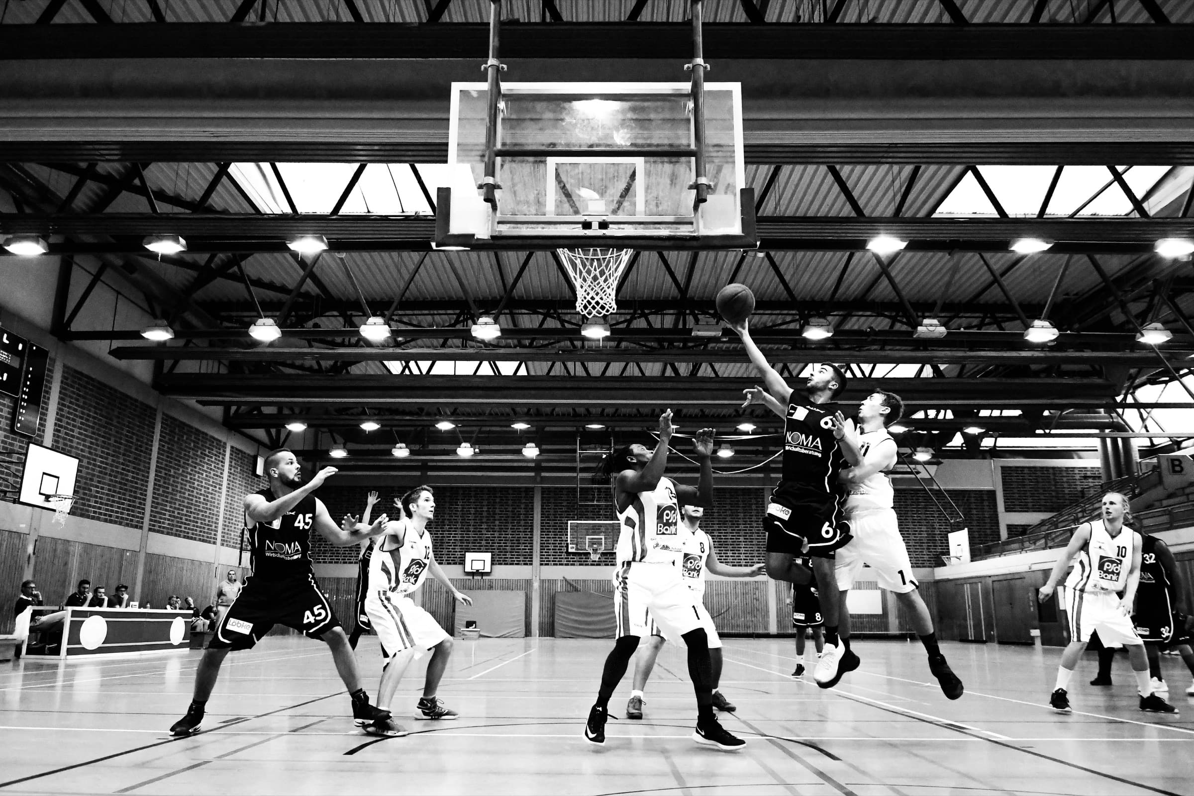 A guard rises for a layup under the basket in a packed high-school gym